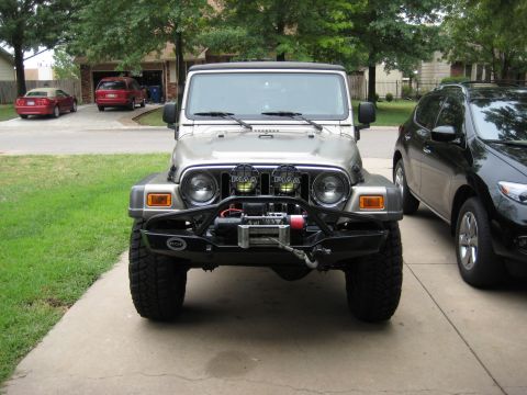 2005 Jeep Wrangler - A silver Jeep Wrangler is parked in a driveway next to a black SUV, with two other vehicles visible in the background.