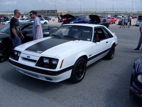 2007 Ford Mustang - A white 1980s Ford Mustang GT is parked at an outdoor event with other vehicles and people around.