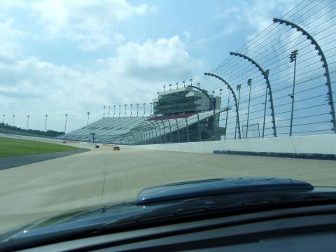 2007 Ford Mustang - A view from a car on a race track shows grandstands and other cars in the distance under a cloudy sky.