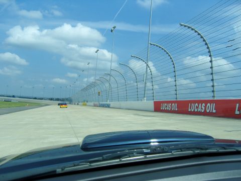 2007 Ford Mustang - A race track scene with two cars visible in the distance, bordered by fences and advertising signs.