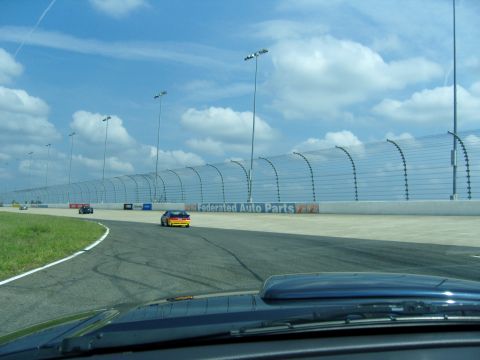 2007 Ford Mustang - A race car speeds around a track under a partly cloudy sky, with a Federated Auto Parts advertisement visible along the barrier.