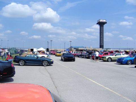 2007 Ford Mustang - A gathering of Ford Mustangs under a partly cloudy sky, with a prominent tower in the distance.