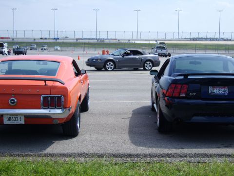 2007 Ford Mustang - An orange 1969 Ford Mustang is parked next to a black Ford Mustang GT at a car show.