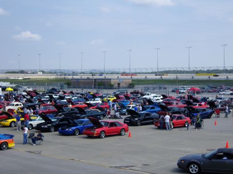 2007 Ford Mustang - A large gathering of Ford Mustangs are on display at an outdoor event, with a racetrack visible in the background.