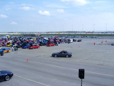 2007 Ford Mustang - A car show event with numerous Ford Mustangs and other vehicles on display under a partly cloudy sky.