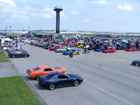 2007 Ford Mustang - A large gathering of Ford Mustangs are on display at an outdoor event, with a prominent tower in the background.