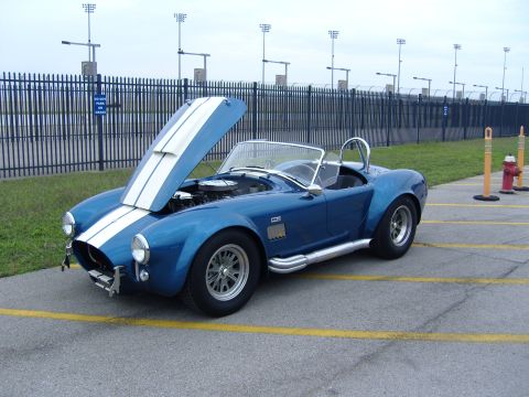 2007 Ford Mustang - A classic blue convertible with white racing stripes is parked with its hood open, revealing the engine.