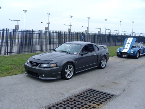 2007 Ford Mustang - A dark gray 2007 Ford Mustang coupe is parked in front of a blue convertible with its hood open.