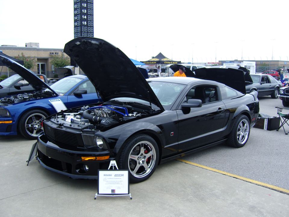 Black 2007 Ford Mustang parked with hood open, showing engine. Blue Mustang also visible