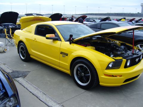 2007 Ford Mustang - A yellow Ford Mustang GT is parked with its hood open at an outdoor car show.