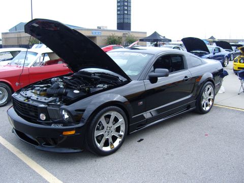 2007 Ford Mustang - A black Ford Mustang is displayed with its hood open, revealing the engine compartment, at an outdoor car show.