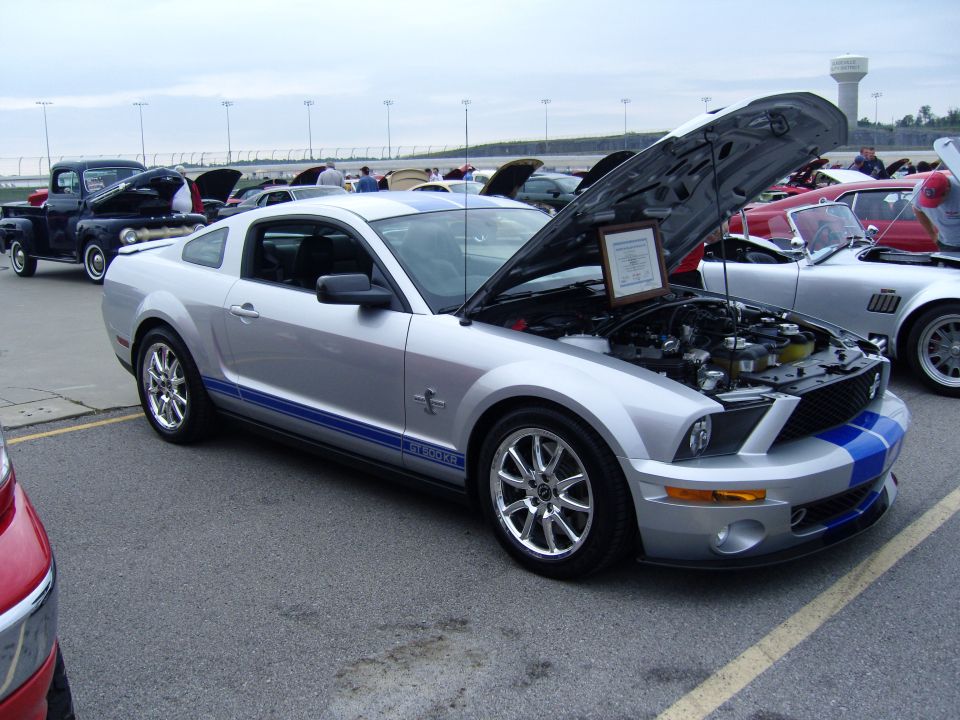 Silver 2007 Ford Mustang GT500 with blue stripes, hood open, parked at a car show