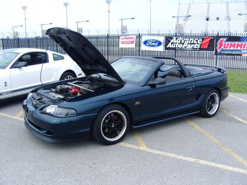 2007 Ford Mustang - Dark green convertible Mustang with hood open, parked next to a white Mustang GT 500.