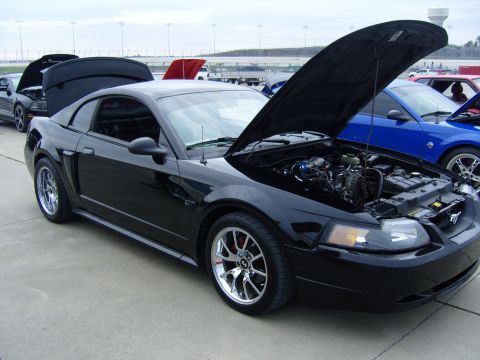 2007 Ford Mustang - A black Mustang is parked with its hood open, revealing the engine bay, alongside other vehicles.