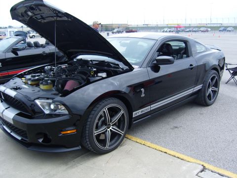 2007 Ford Mustang - A black Ford Mustang GT500 is parked with its hood open, revealing the engine bay and silver racing stripes.