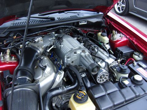 2007 Ford Mustang - Engine bay detail shot with a supercharger prominently displayed; another vehicle is partially visible.