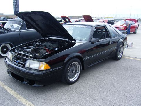 2007 Ford Mustang - This black Ford Mustang, likely from the late 1980s, is displayed with its hood open at an outdoor car show.