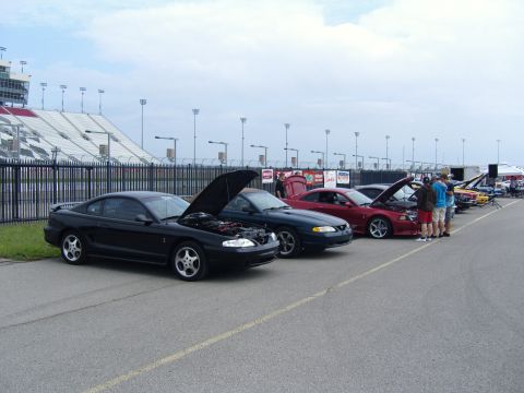 2007 Ford Mustang - Several Mustangs are lined up at a racetrack, with hoods open, under a cloudy sky.