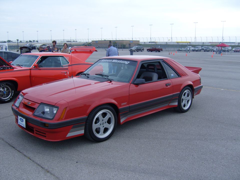 Red coupe car with a spoiler and racing stripes, parked on asphalt