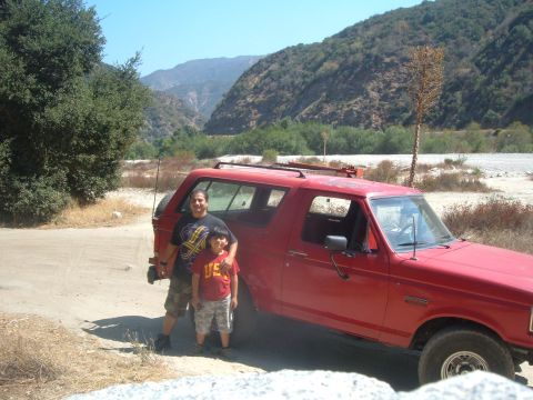 1988 Ford Bronco - A red 1987 Ford Bronco is parked on a dirt road in a mountainous area with two people standing beside it.