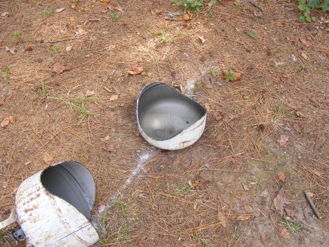 1978 Ford Bronco - Two damaged metal helmet pieces are scattered on a pine needle-covered ground.
