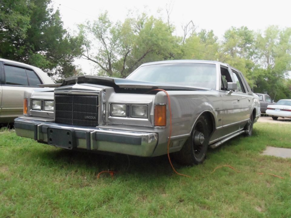 Silver Lincoln Town Car with hood open, missing front passenger wheel, parked on grass