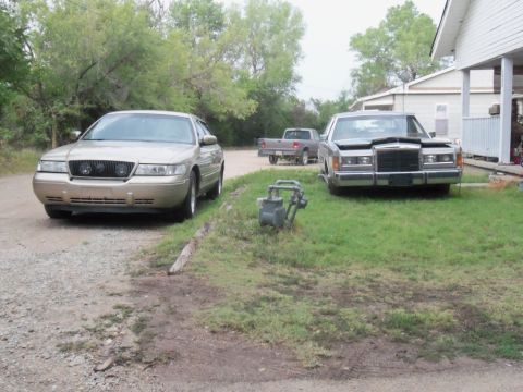 2000 Mercury Grand Marquis - Two sedans and a pickup truck are parked in a yard with trees and a house.