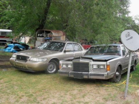 2000 Mercury Grand Marquis - Two sedans are parked on a grassy area with trees in the background and a satellite dish to the right.
