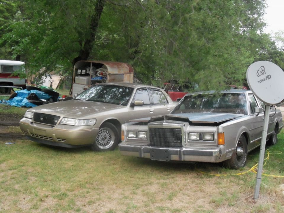 Gold sedan with a black grille and chrome wheels, parked next to a silver sedan with its hood open