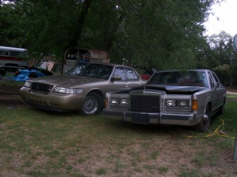 2000 Mercury Grand Marquis - Two large sedans, a Mercury Grand Marquis and a Lincoln Town Car, sit parked in a yard.
