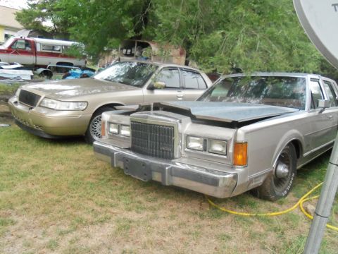 2000 Mercury Grand Marquis - Two sedans are parked in a grassy area with trees in the background.