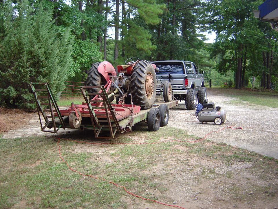 Silver pickup truck towing a trailer with a tractor and an air compressor