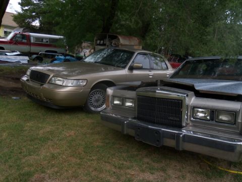 2000 Mercury Grand Marquis - A gold sedan, likely a Mercury Grand Marquis, is parked next to another sedan, possibly a Lincoln, in an outdoor setting.