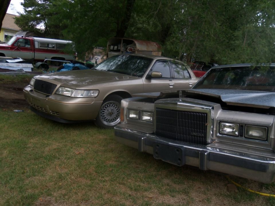 Gold sedan with a black grille and mesh wheels, parked next to a silver sedan with a chrome grille. Both are seen from the front