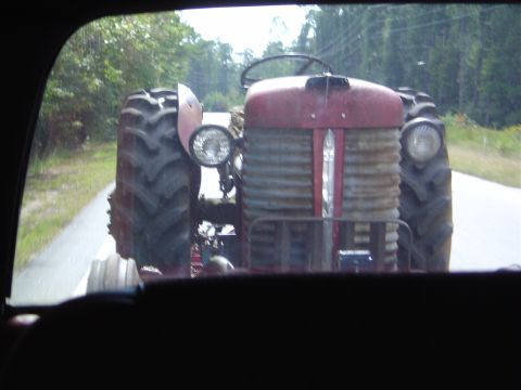1986 Ford Bronco - A red tractor is seen driving down a paved road, surrounded by trees.