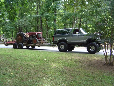 1986 Ford Bronco - 1986 Ford Bronco is seen towing a tractor on a trailer.