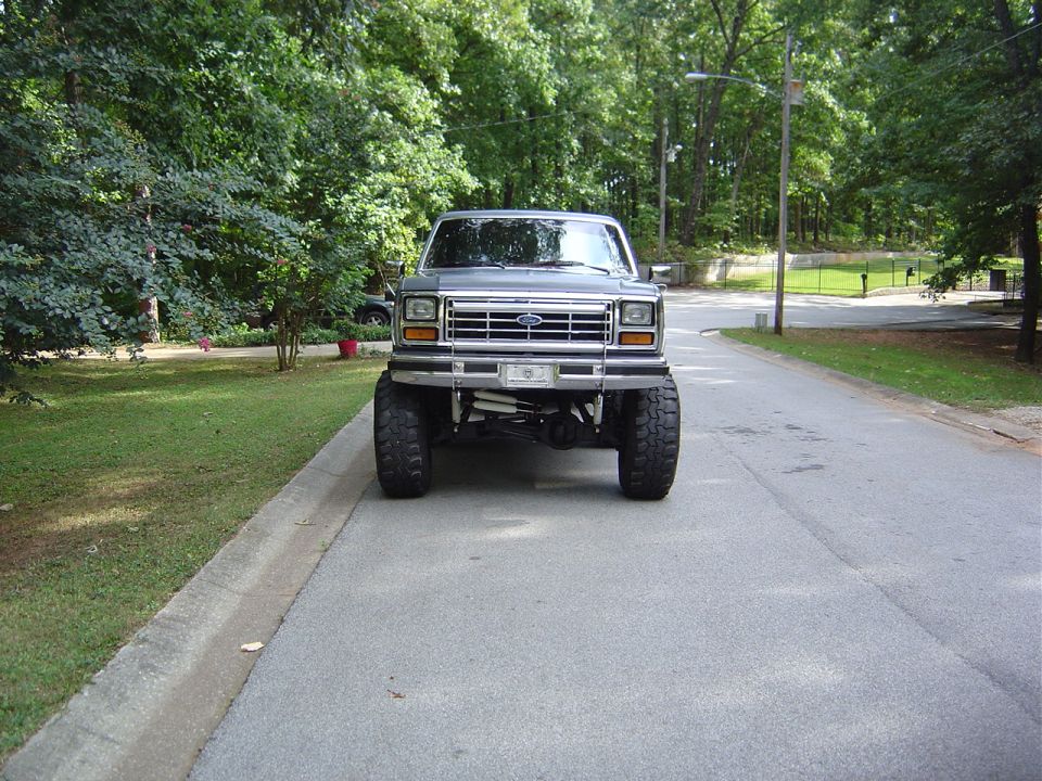 Front view of a lifted gray Ford truck with large tires parked on a residential street