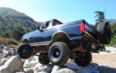 1986 Ford Bronco - A modified 1992 Ford Bronco is shown off-roading over large rocks on a sunny day.