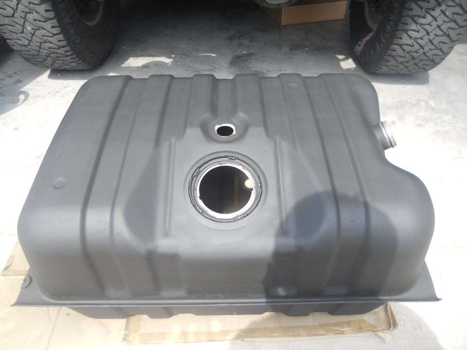 Fuel tank with mounting flange and filler neck opening. Tire and undercarriage of a vehicle visible above