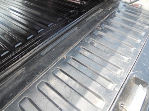 1991 Ford Bronco - Close-up of a worn black ribbed truck bed liner, showing the texture and some scratches.