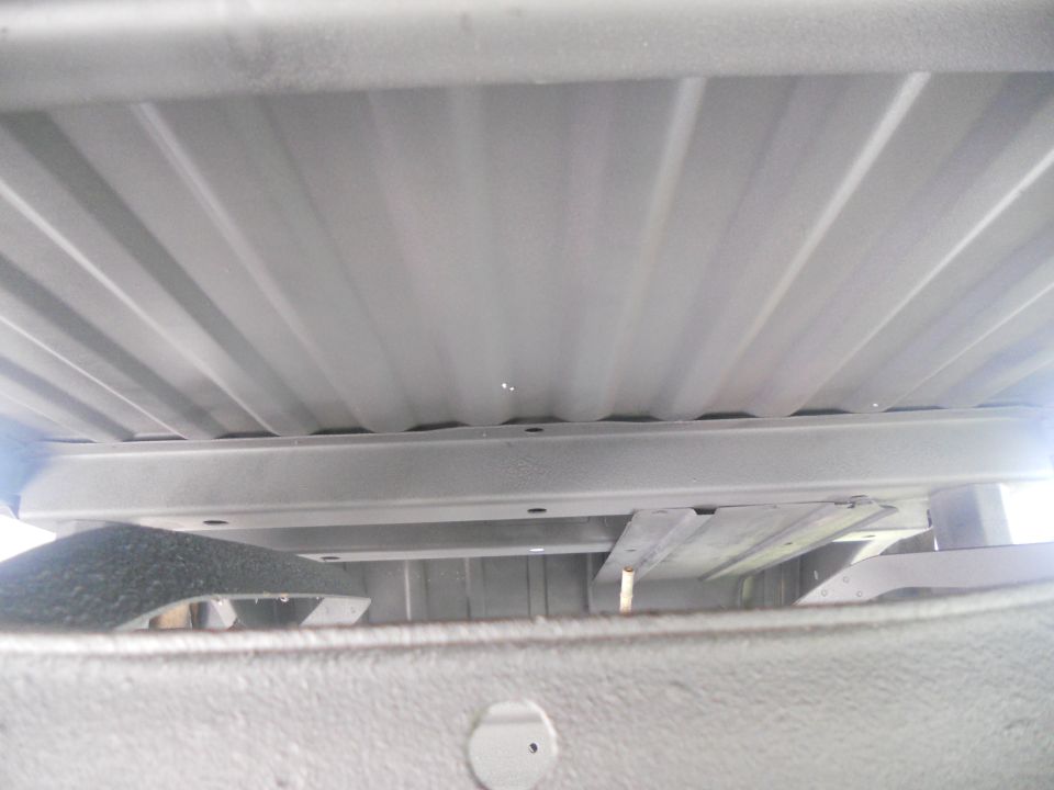 Underside of a gray vehicle bed with visible crossbeams and corrugated metal