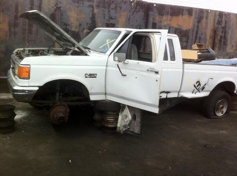 1992 Ford Bronco - White Ford F-250 pickup truck with hood and driver door open, missing front wheels, on tires.