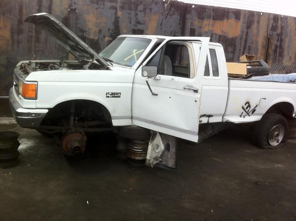 White Ford F-250 pickup truck with hood and driver door open, missing front wheels, on tires