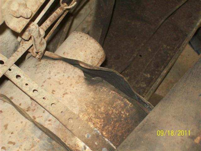 Underside of a vehicle showing a damaged exhaust pipe and rusty metal components