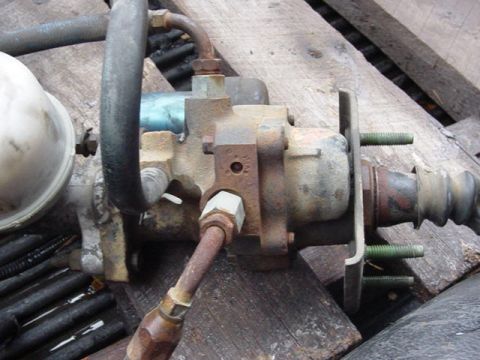 1992 Ford Bronco - Close-up of a used hydroboost brake booster unit lying on a wood pallet, its cast body surface-rusted with hydraulic hose fittings, a mount…