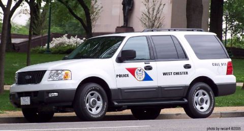 2006 Ford F-150 - A white police SUV, marked 'West Chester', is parked on a street with trees and a building in the background.