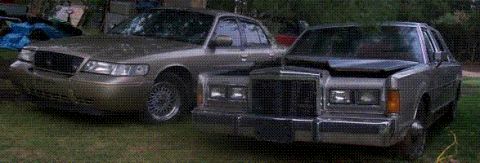 2000 Mercury Grand Marquis - Two older model sedans are parked side-by-side on a grassy area with trees in the background.