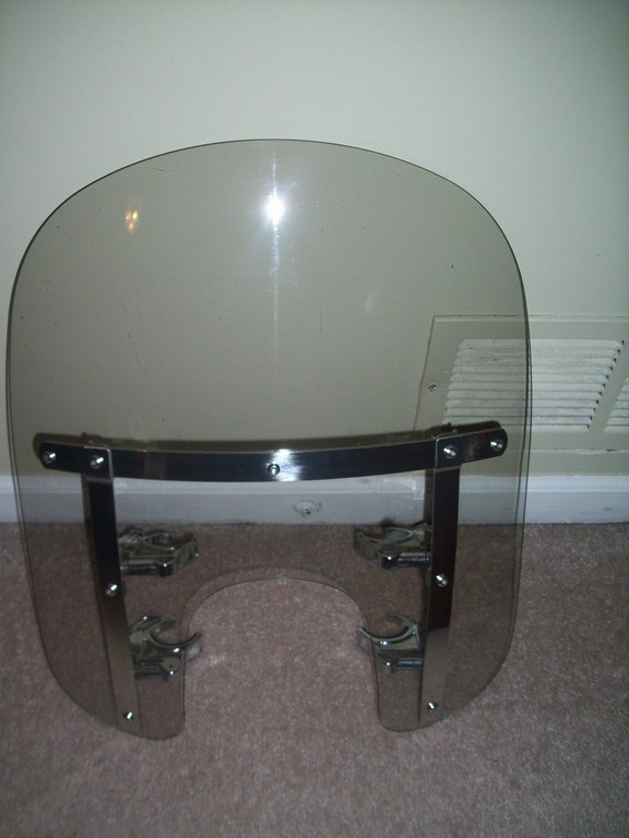Motorcycle windshield with chrome mounting hardware, tinted plastic, on carpet