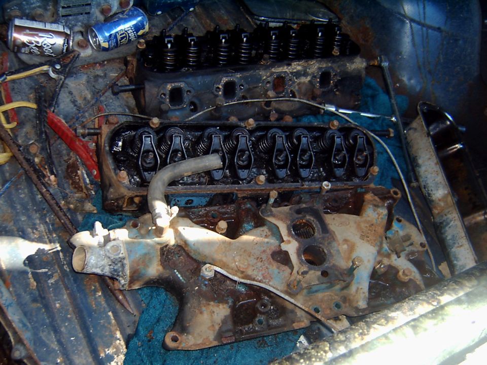 Two V8 cylinder heads with rockers and a rusty cast intake manifold laid out on carpet