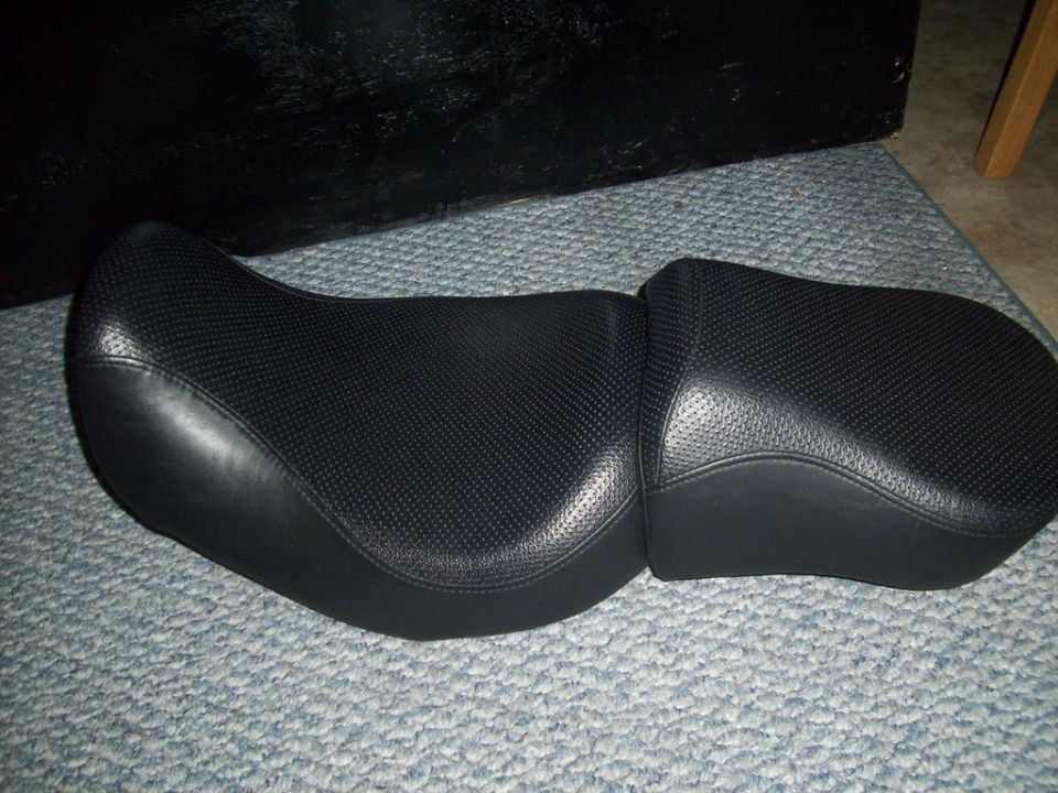 Black two-up motorcycle seat with perforated centers sitting on carpet, removed from bike